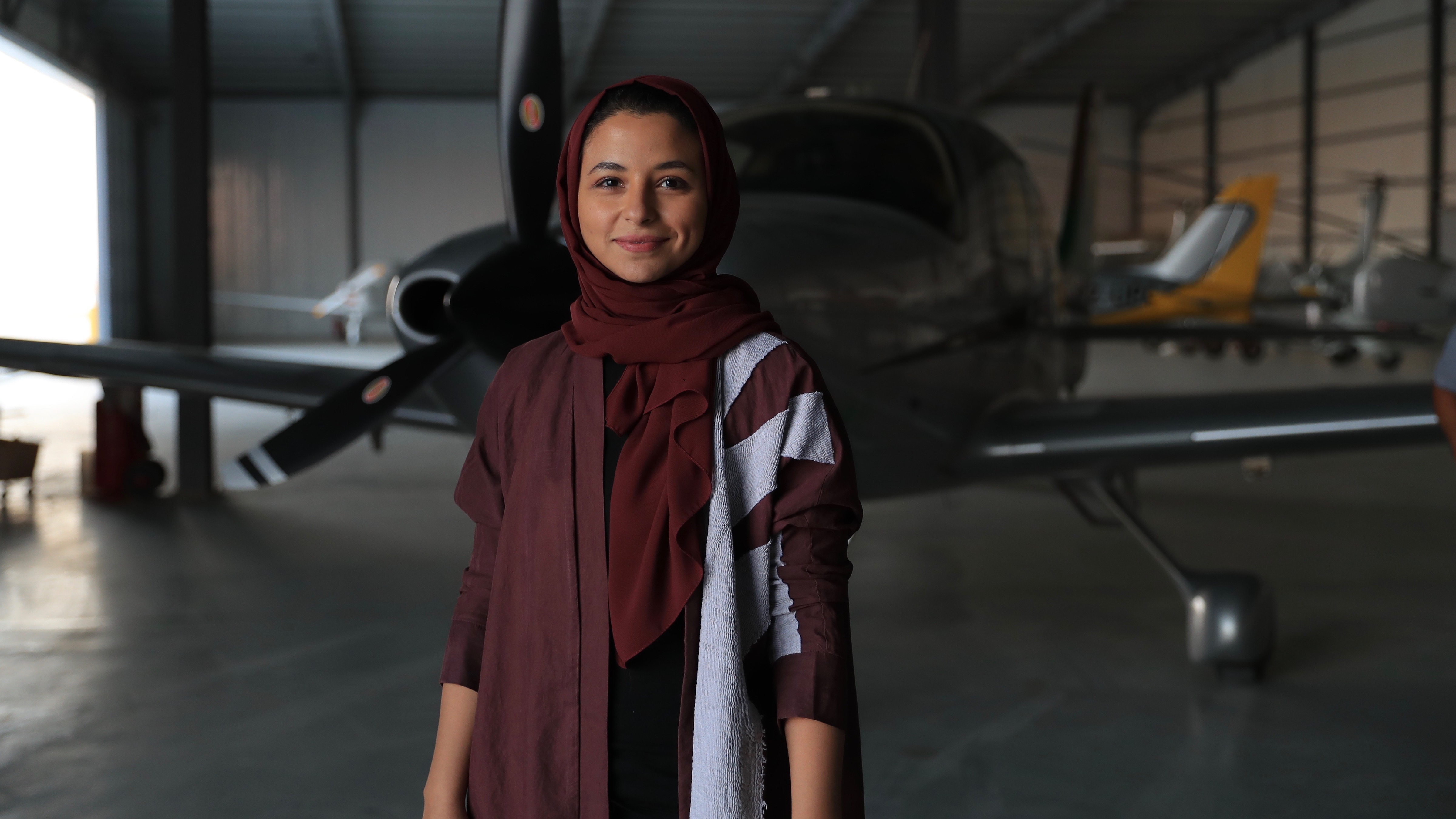 Smiling woman in hijab with small light aircraft behind her