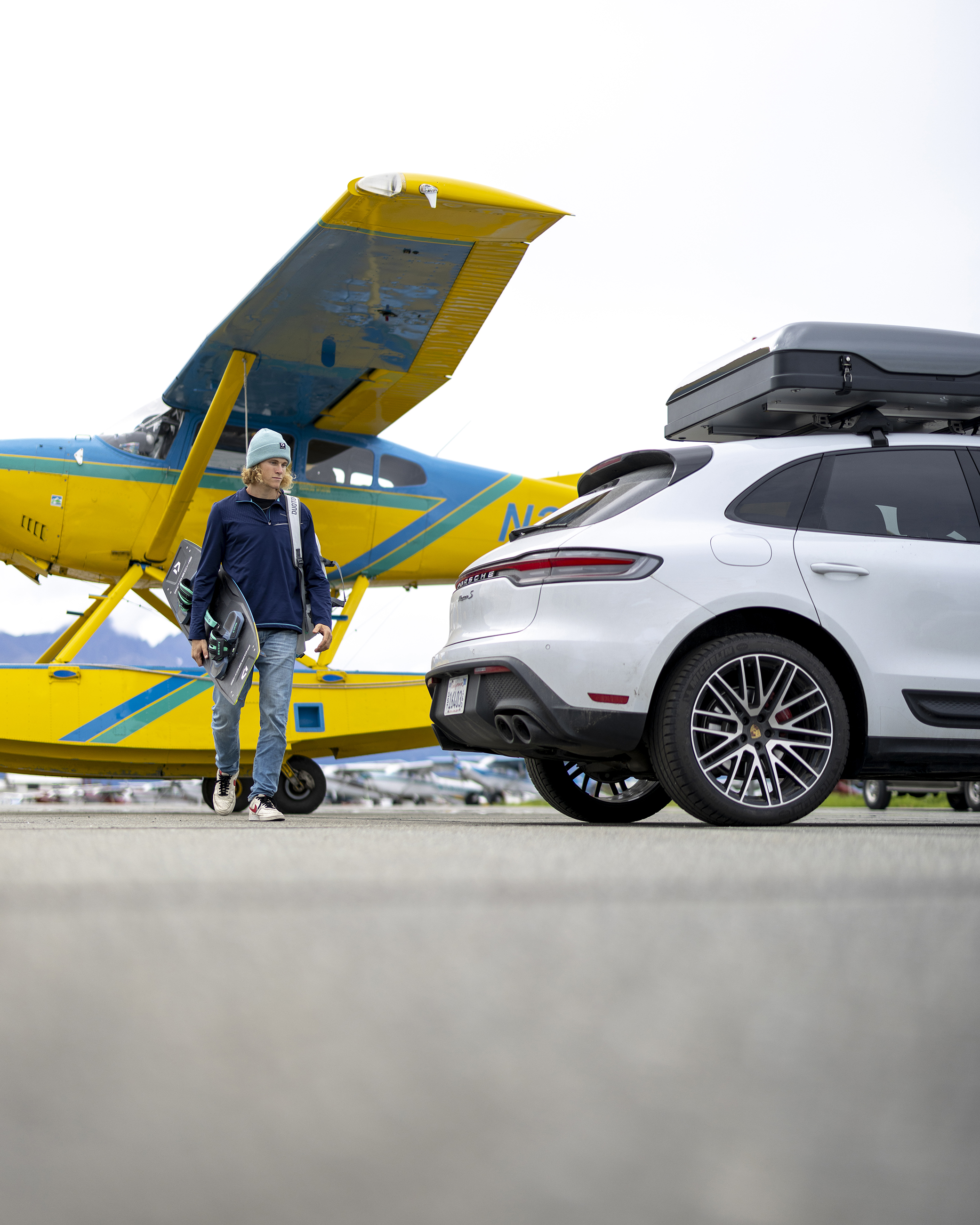 Kitesurfer Liam Whaley walking from yellow seaplane to Porsche Macan