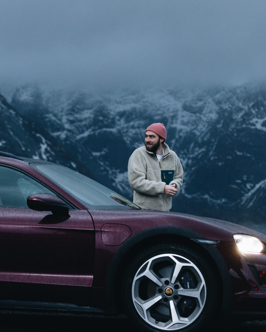 Man stands behind Taycan Cross Turismo, snow-topped mountains in background