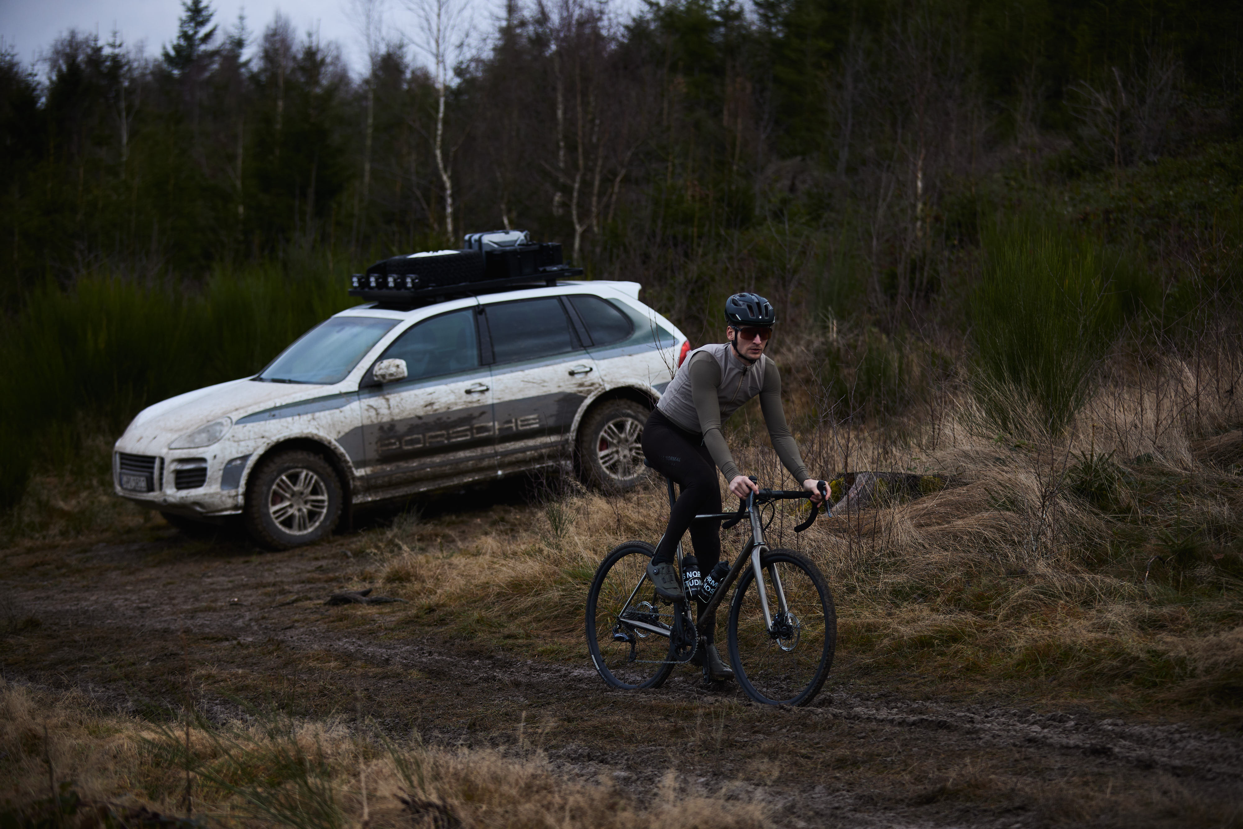 Cyclist on gravel bike in front of classic Cayenne in forest