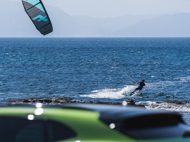 Man carrying kitesurfing kite, sea behind, green Porsche in shot