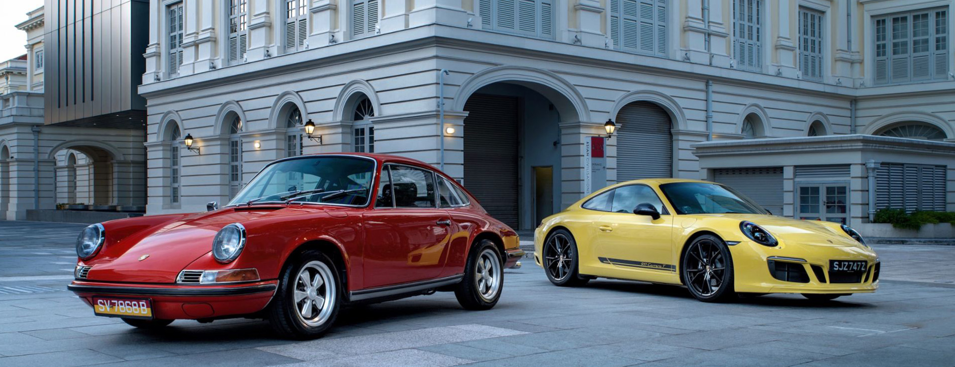 Guards Red and Racing Yellow Porsche cars in front of building