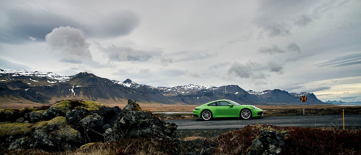 Green Porsche in front of mountains on a cloudy day