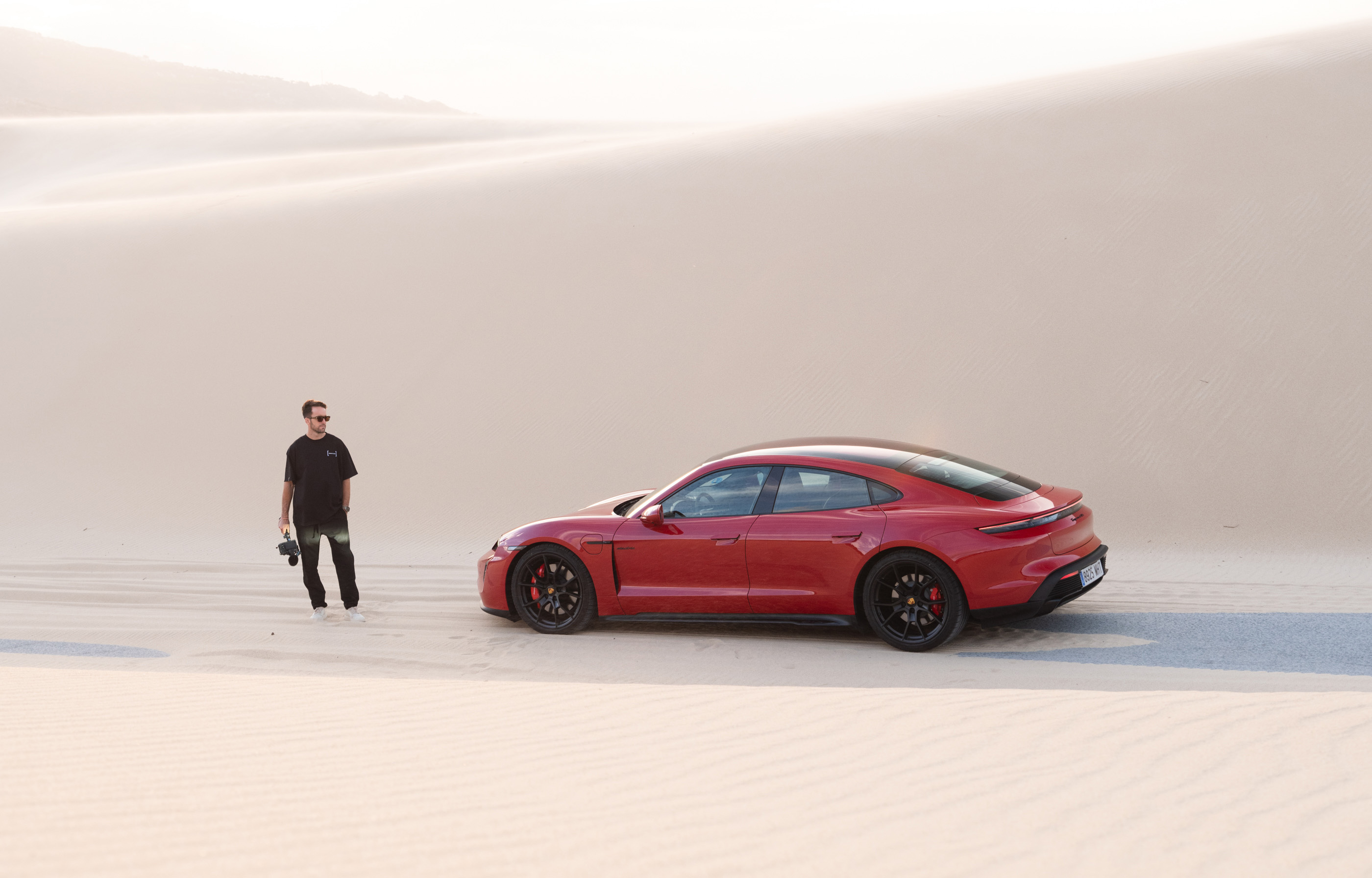 Man stands next to red Porsche Taycan in sand dunes