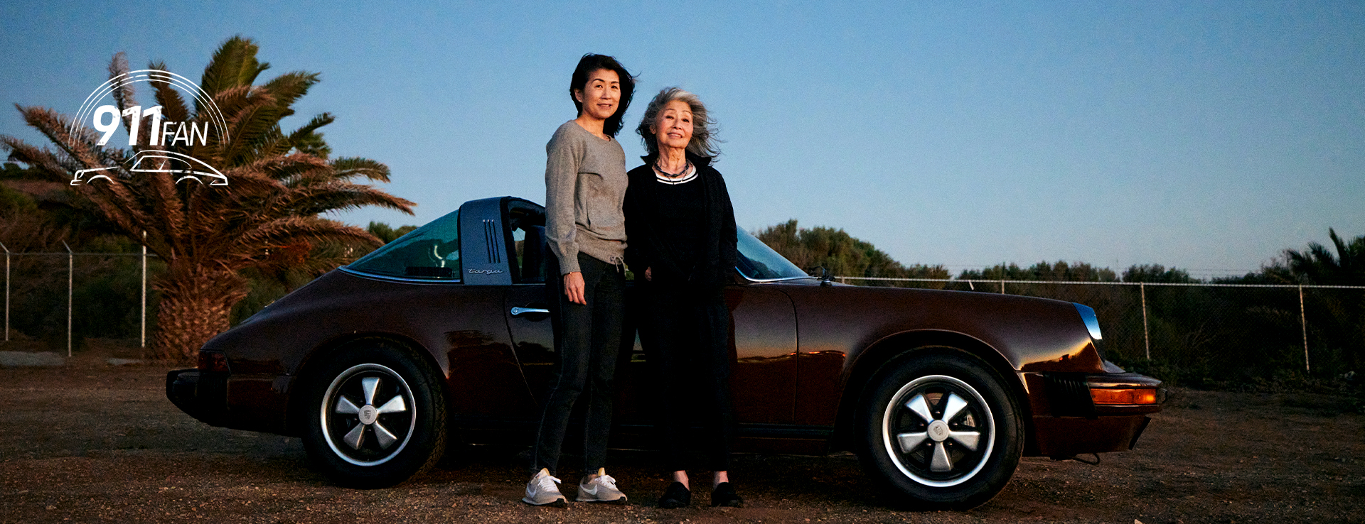 Two women with classic brown Porsche 911 Targa at dusk