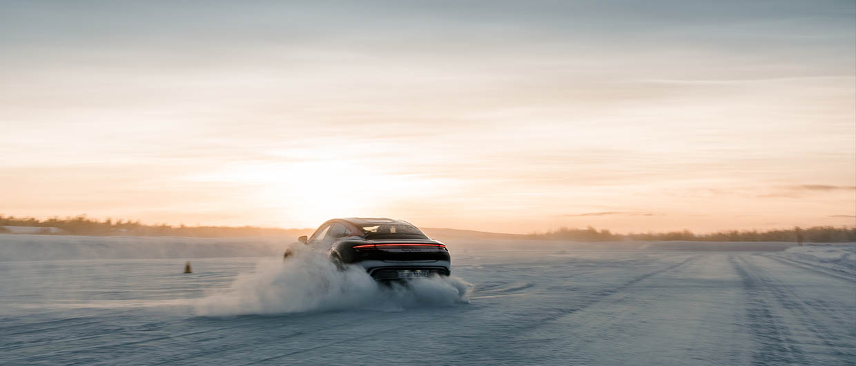 Dark Porsche Taycan drives on ice and snow. Low sun