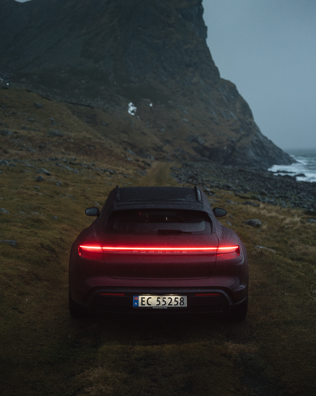 Rear of Taycan Cross Turismo, lights on, against rugged mountains