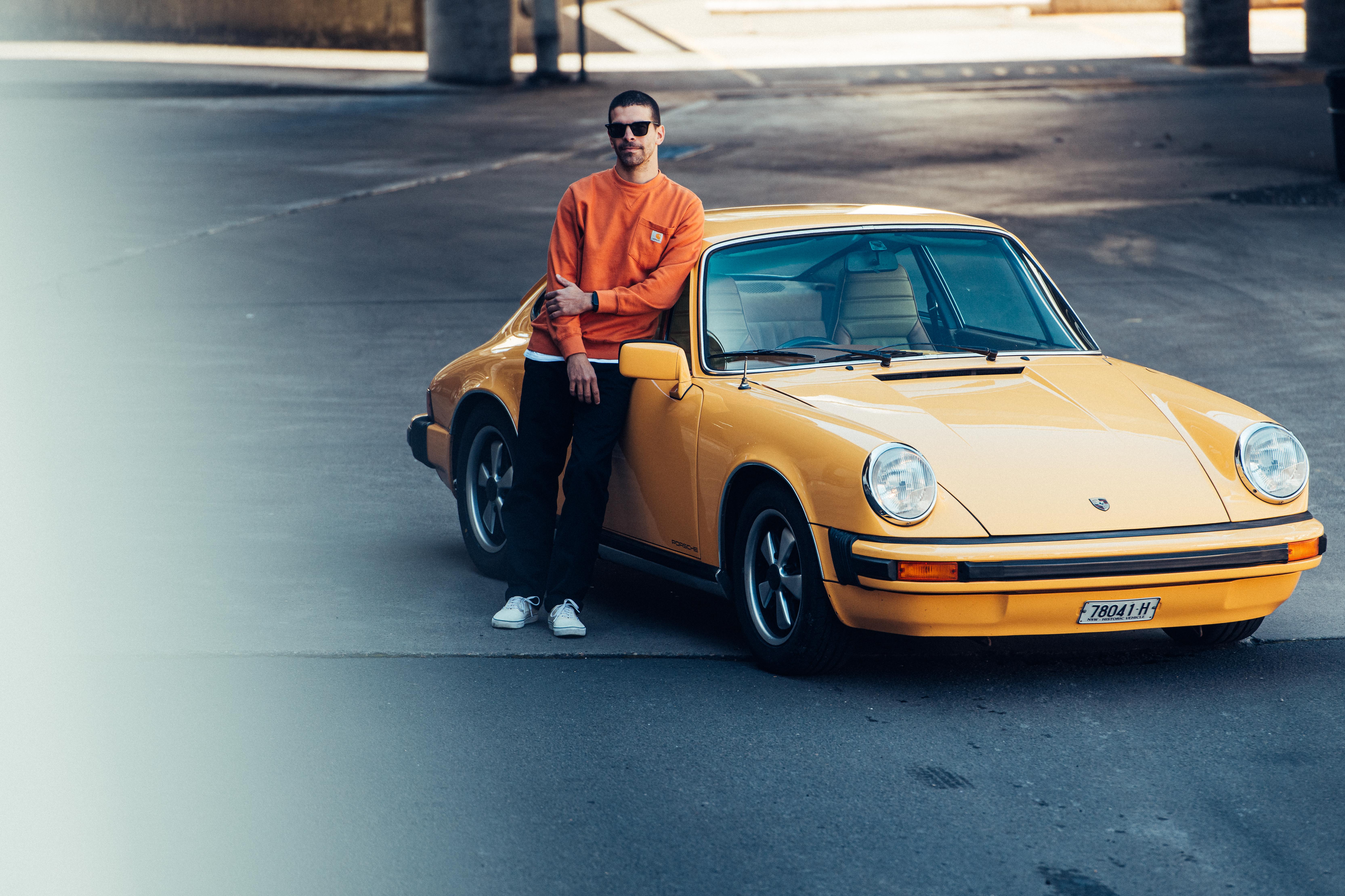 Man in orange jumper leans again classic yellow Porsche