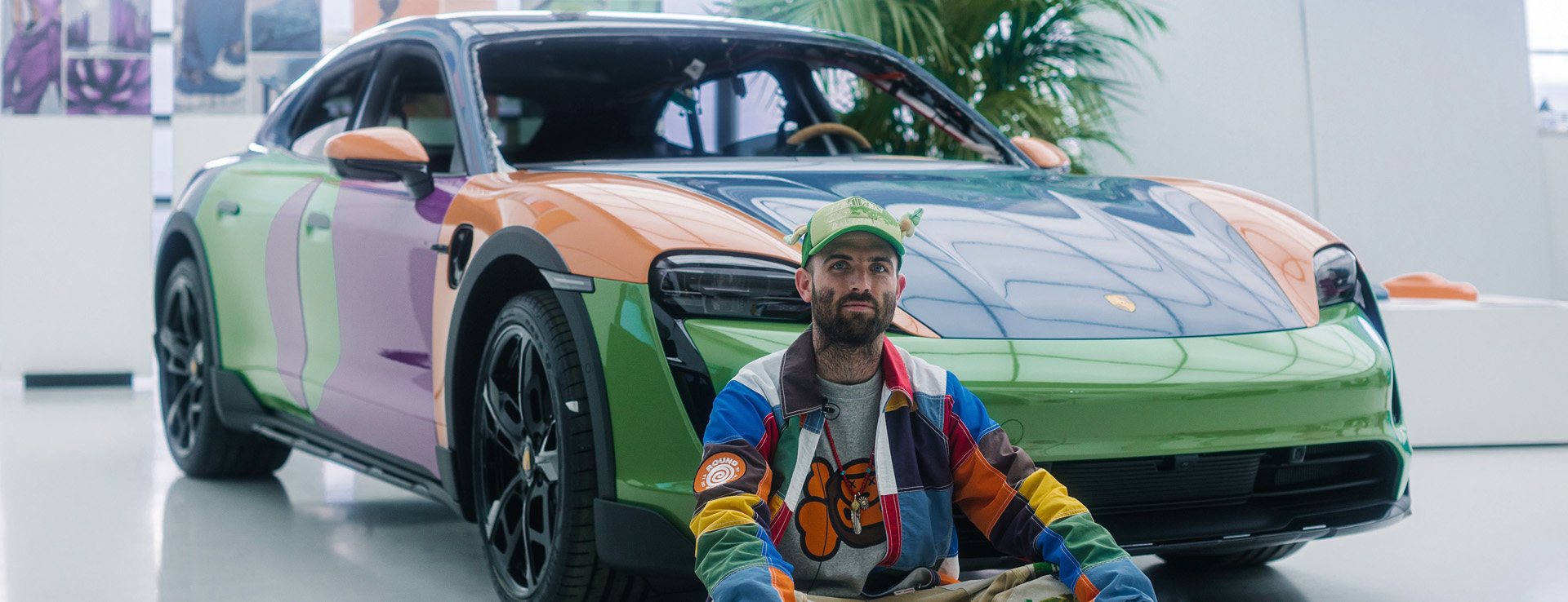 Man in multicoloured jacket sits in front of multicoloured Porsche