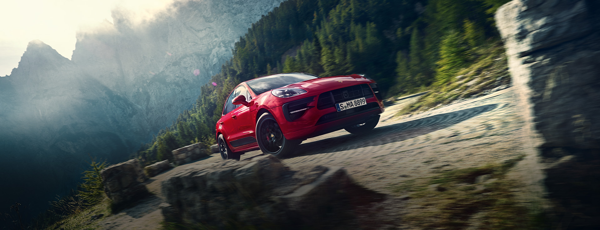 Red Macan GTS on cobbled road, cloudy sunlit mountain behind