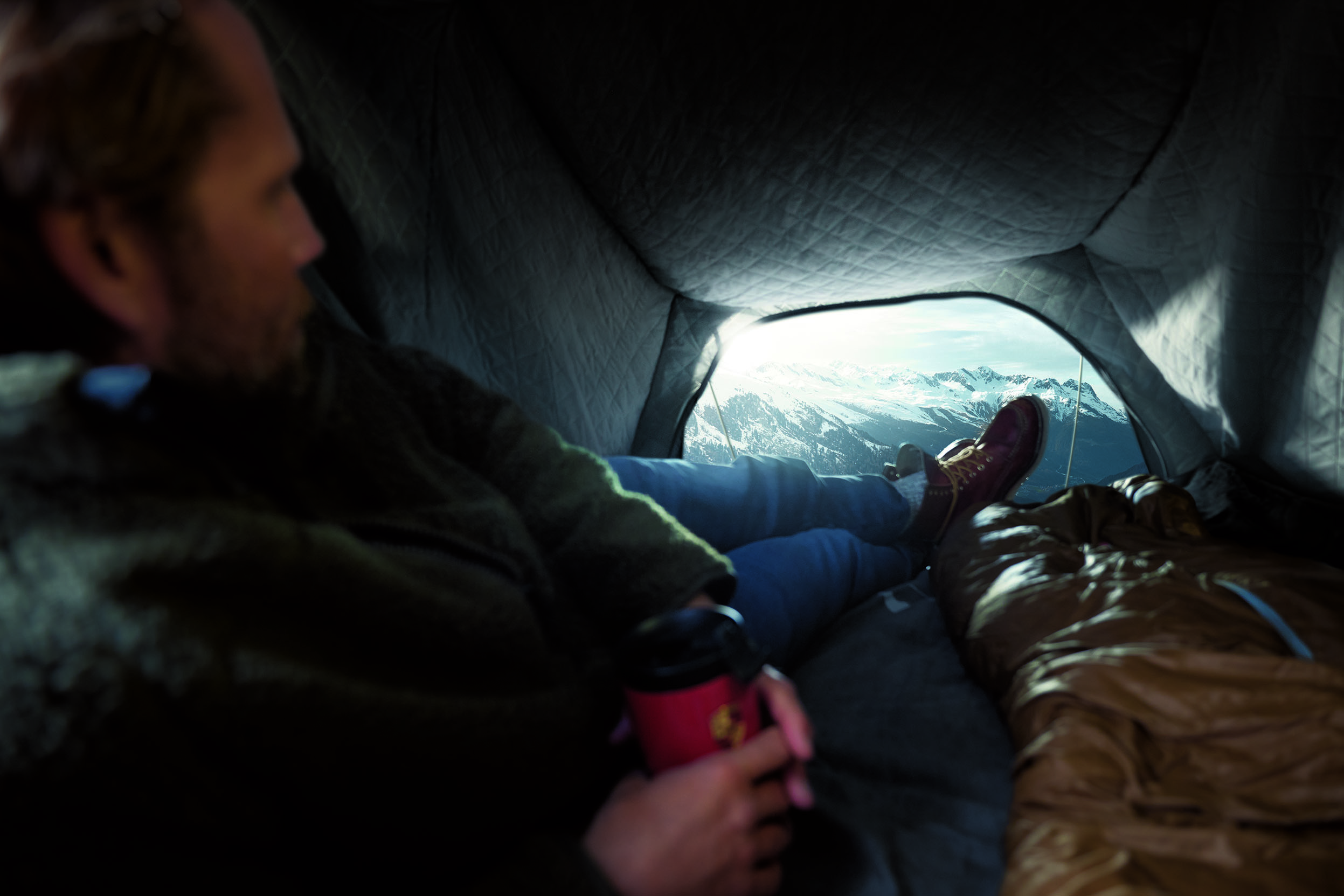 Man lying in Porsche roof tent, view of snowy mountains