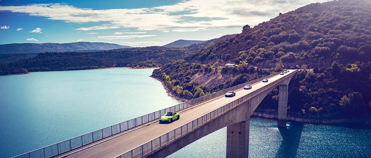 Porsche cars drive over a coastal bridge in Southern France