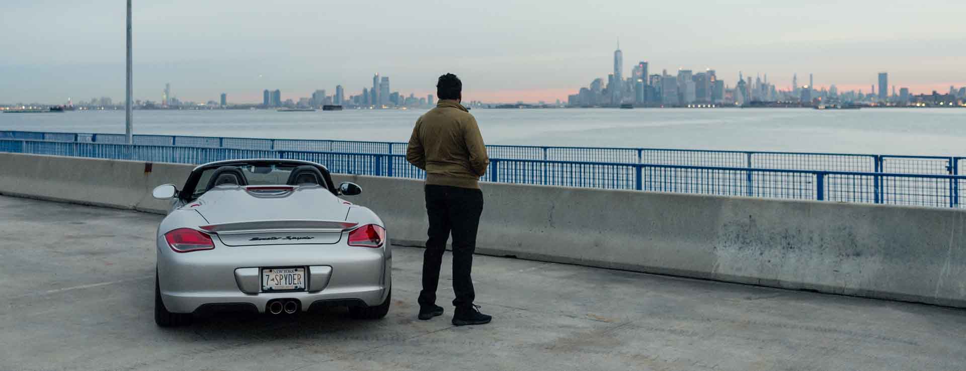 Man standing beside Porsche Boxster Spyder, overlooking New York City