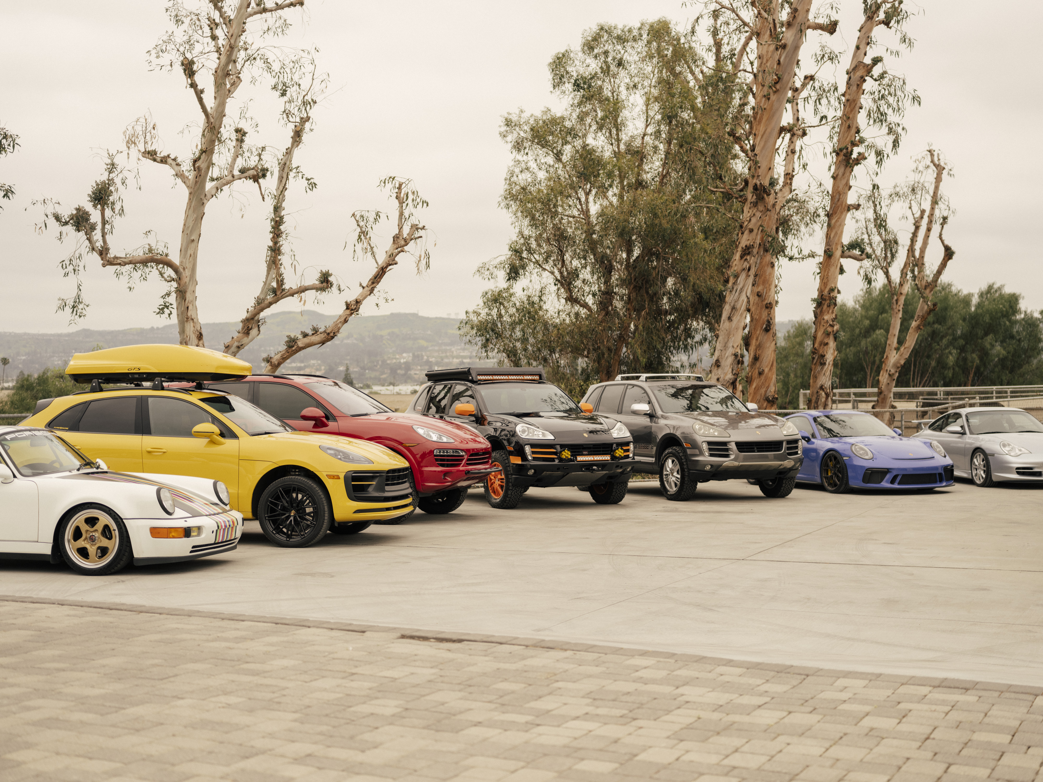 Line-up of Porsche 911 sportscars and Cayenne SUVs outside ranch