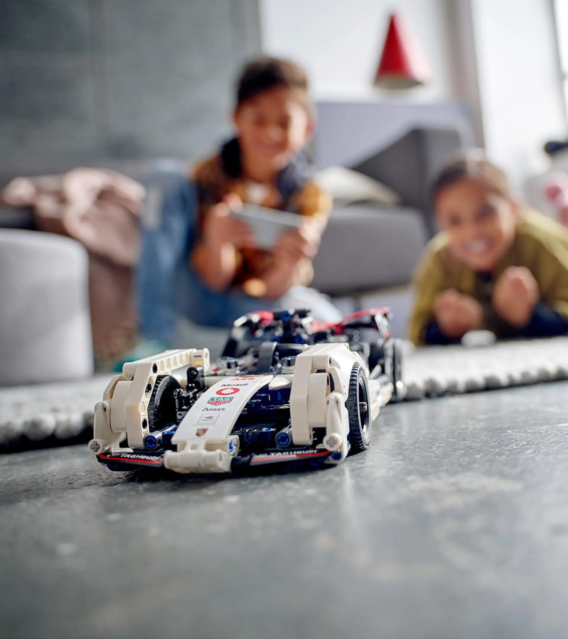 LEGO Porsche on living floor, two children smiling in background