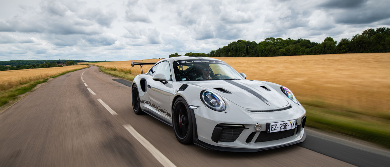 A Porsche 911 GT3 RS drives on road through wheatfields