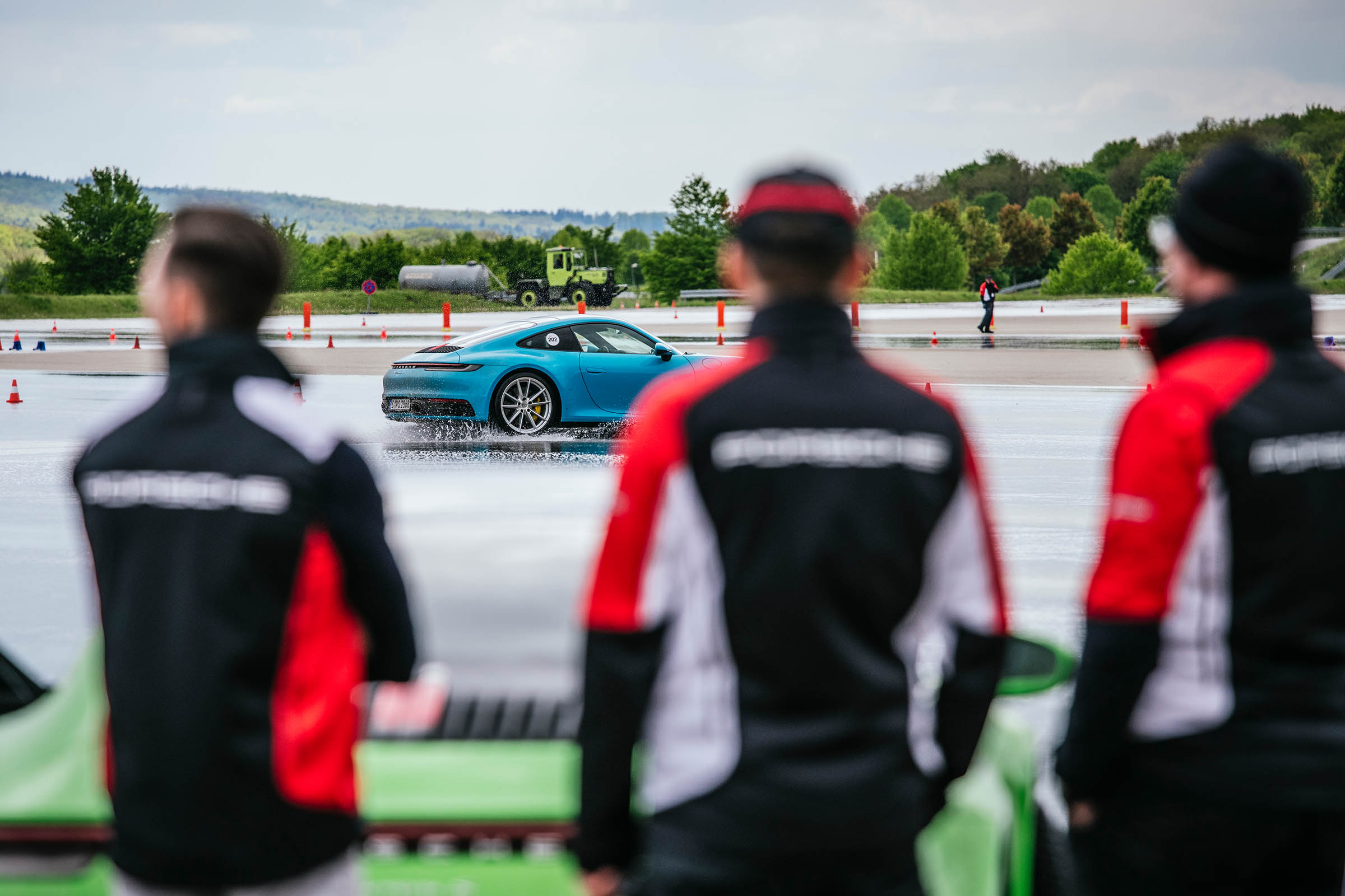 Three Porsche instructors observe as light blue 911 passes by