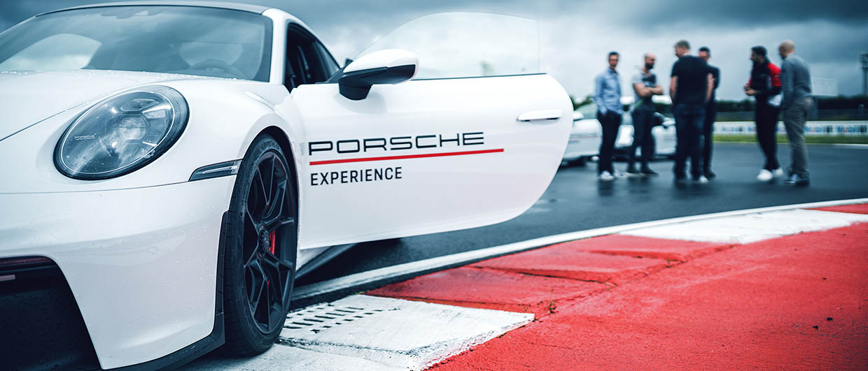 Porsche Experience lettering on the car door, in the background there are a few people on the racetrack