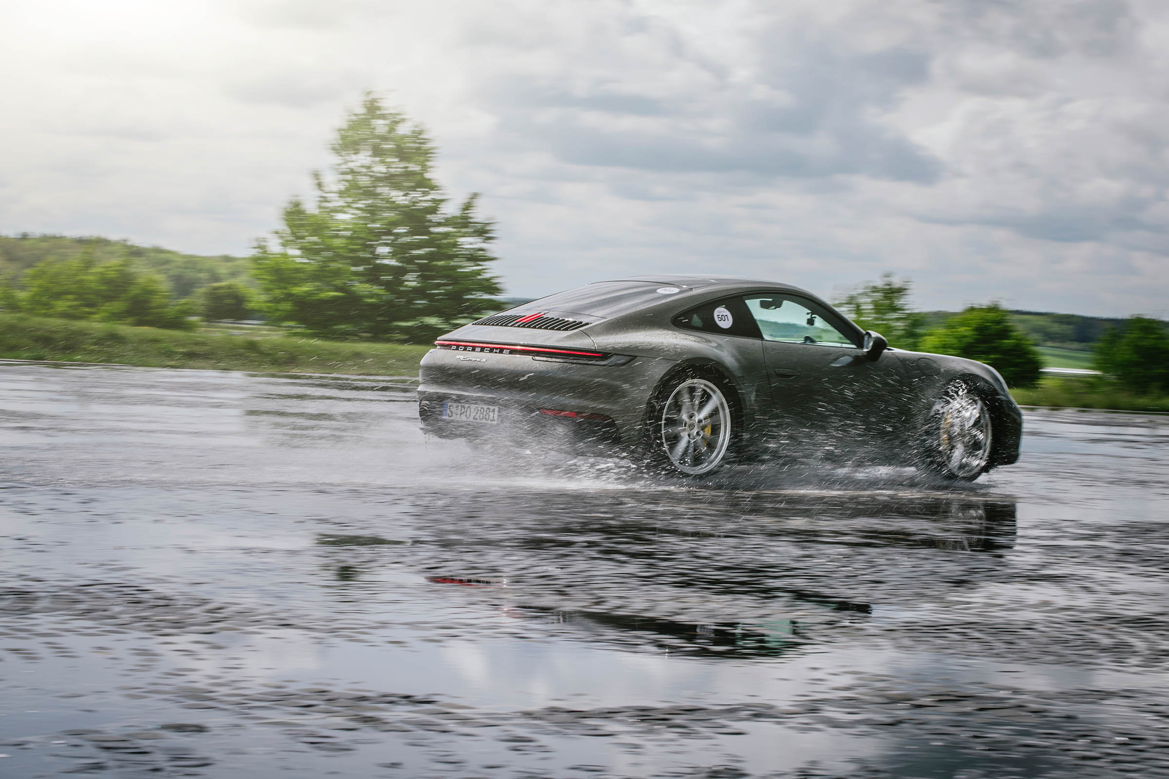 Green Porsche 911 splashing through wet handling circuit at speed