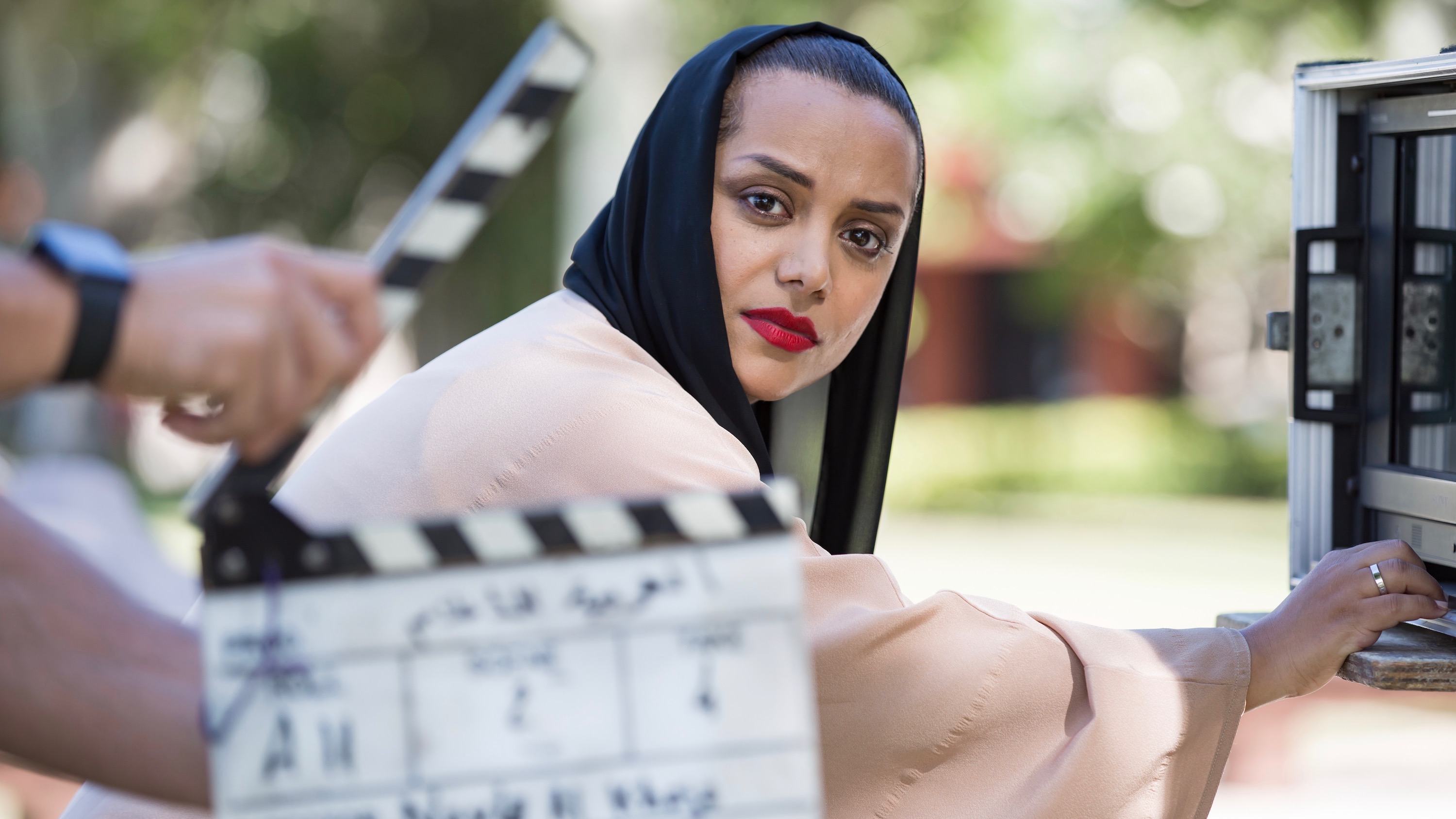 Woman in hijab looks at camera with clapperboard in foreground