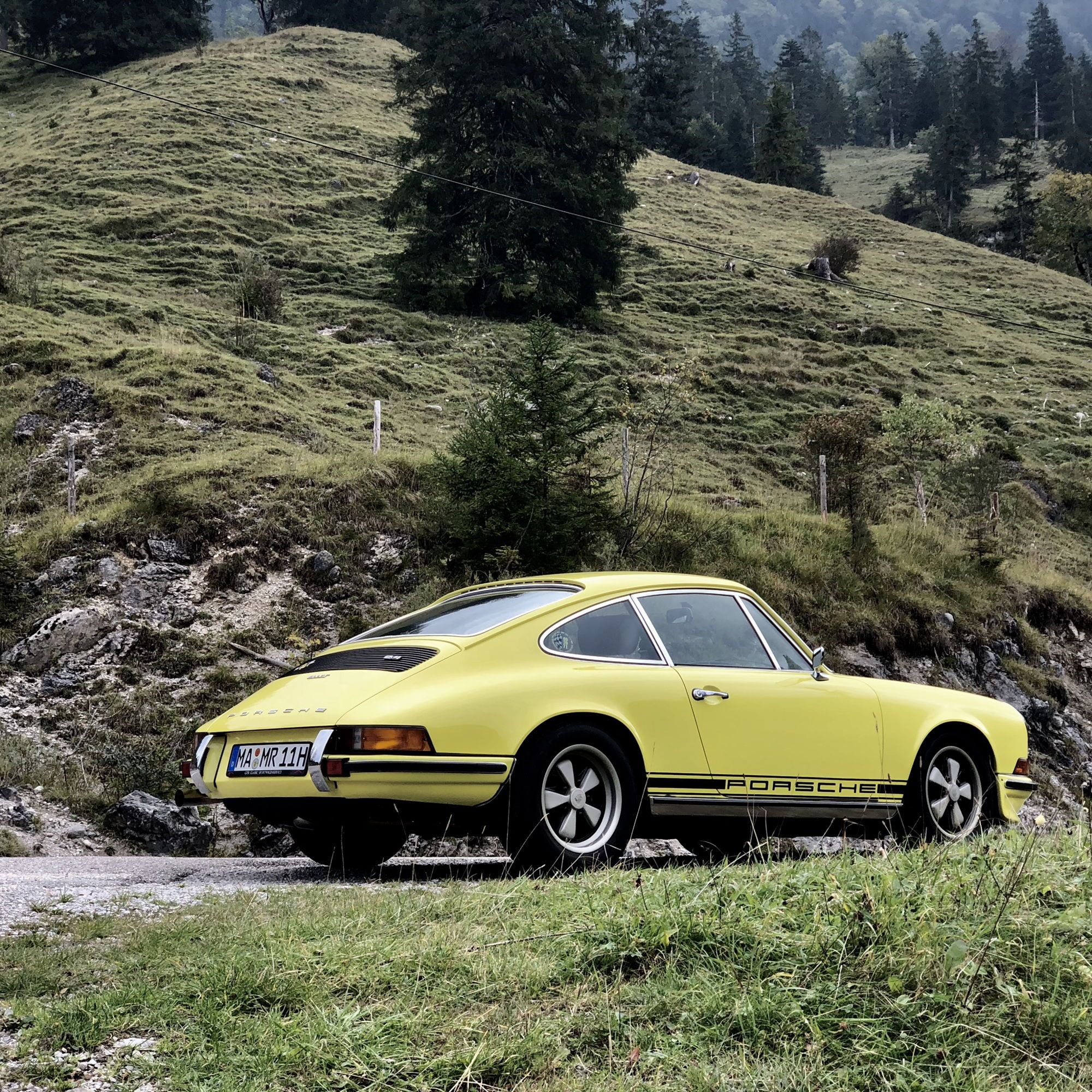 Rear view of yellow 911 F Model parked in woodland