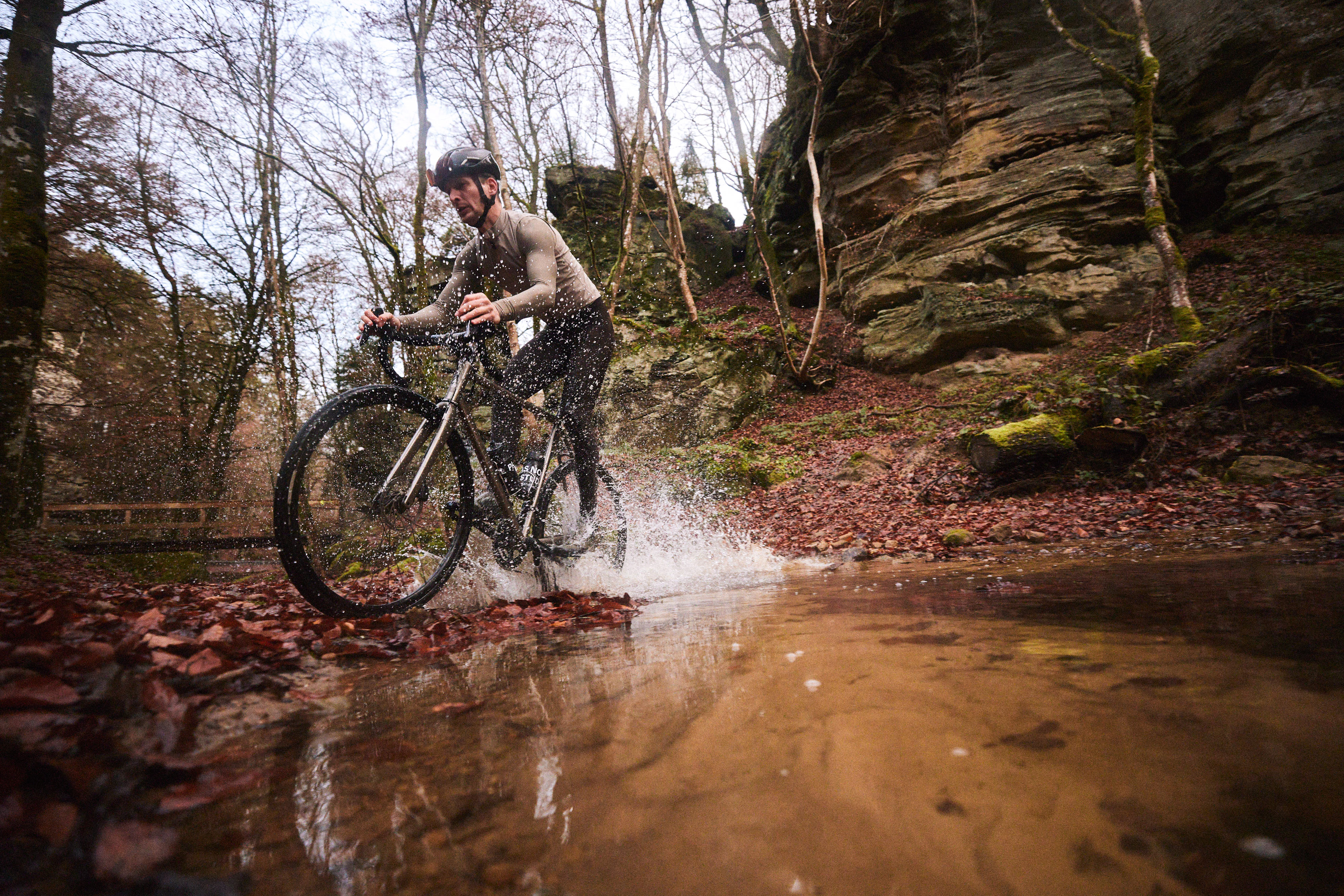Gravel biker riding through muddy puddle in secluded forest