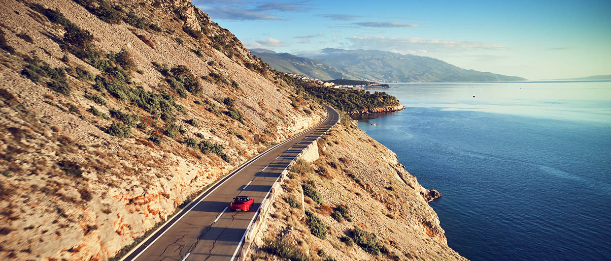 Red Porsche Cabriolet is driving on coastal road in Croatia