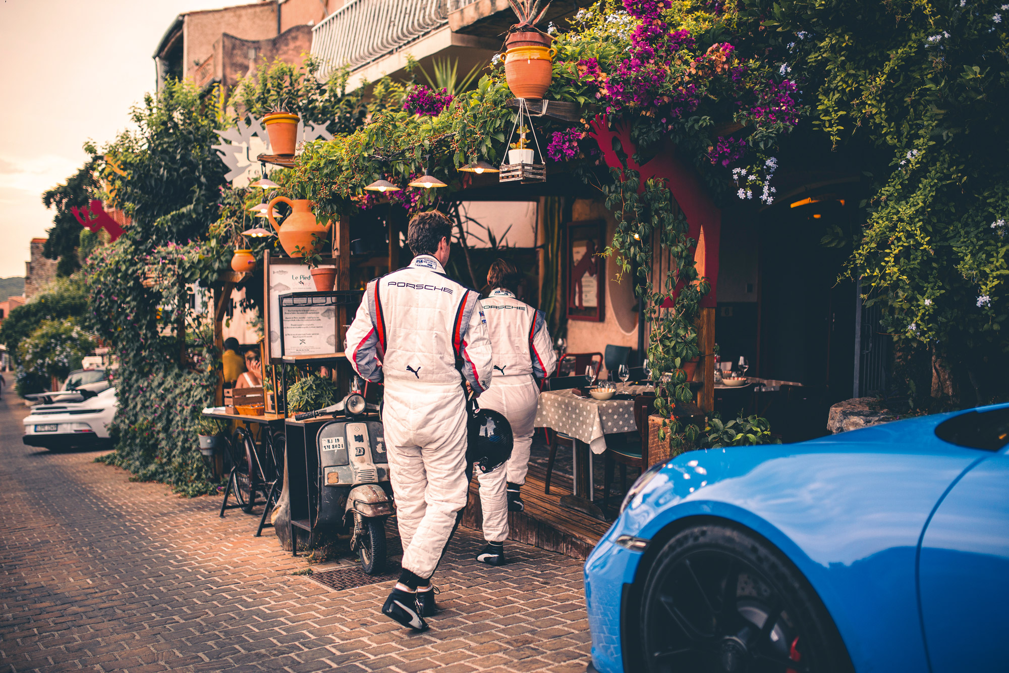 Two men in Porsche racesuits walking into a French restaurant