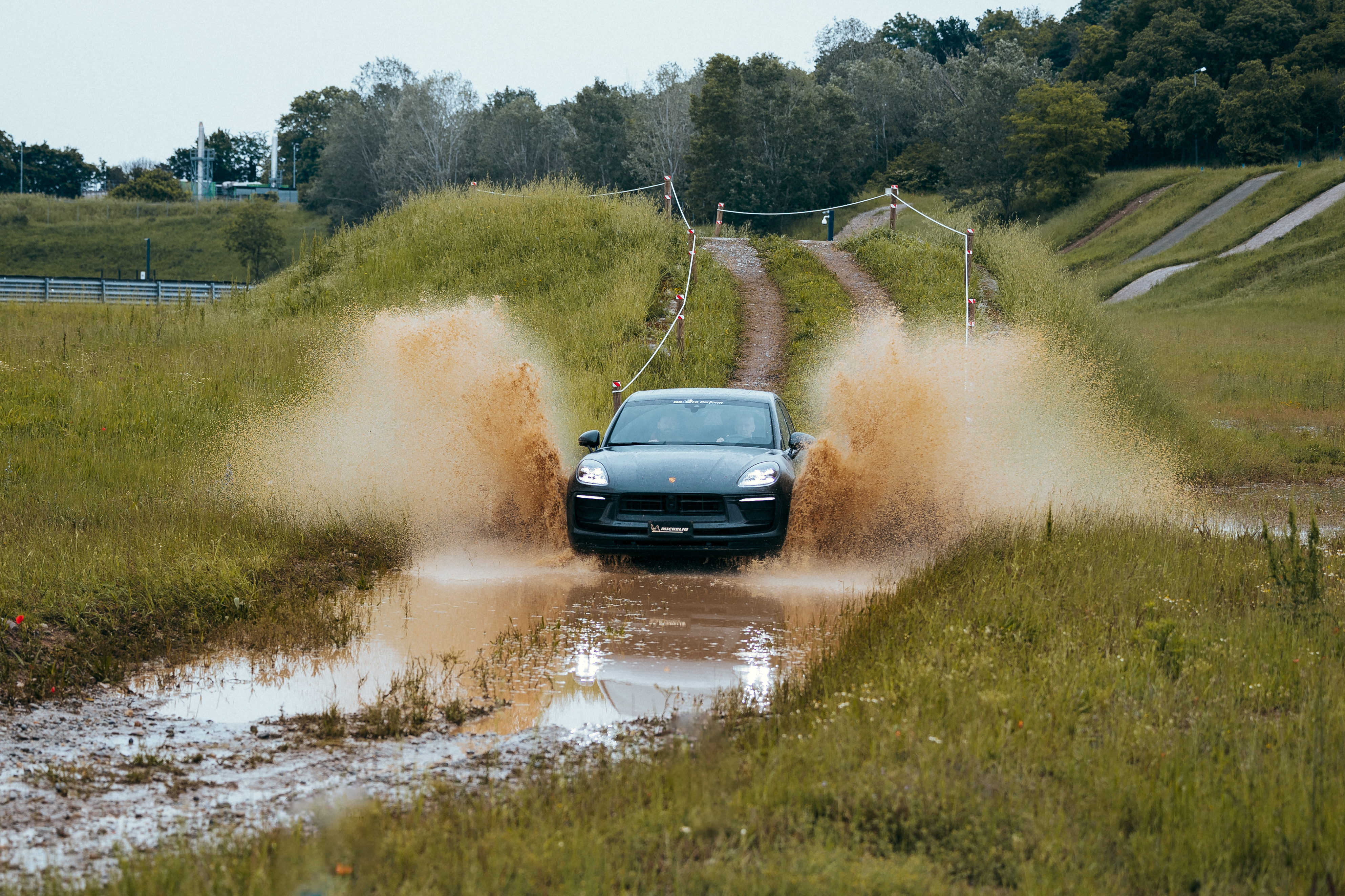 Porsche Cayenne drives down a muddy road into a puddle
