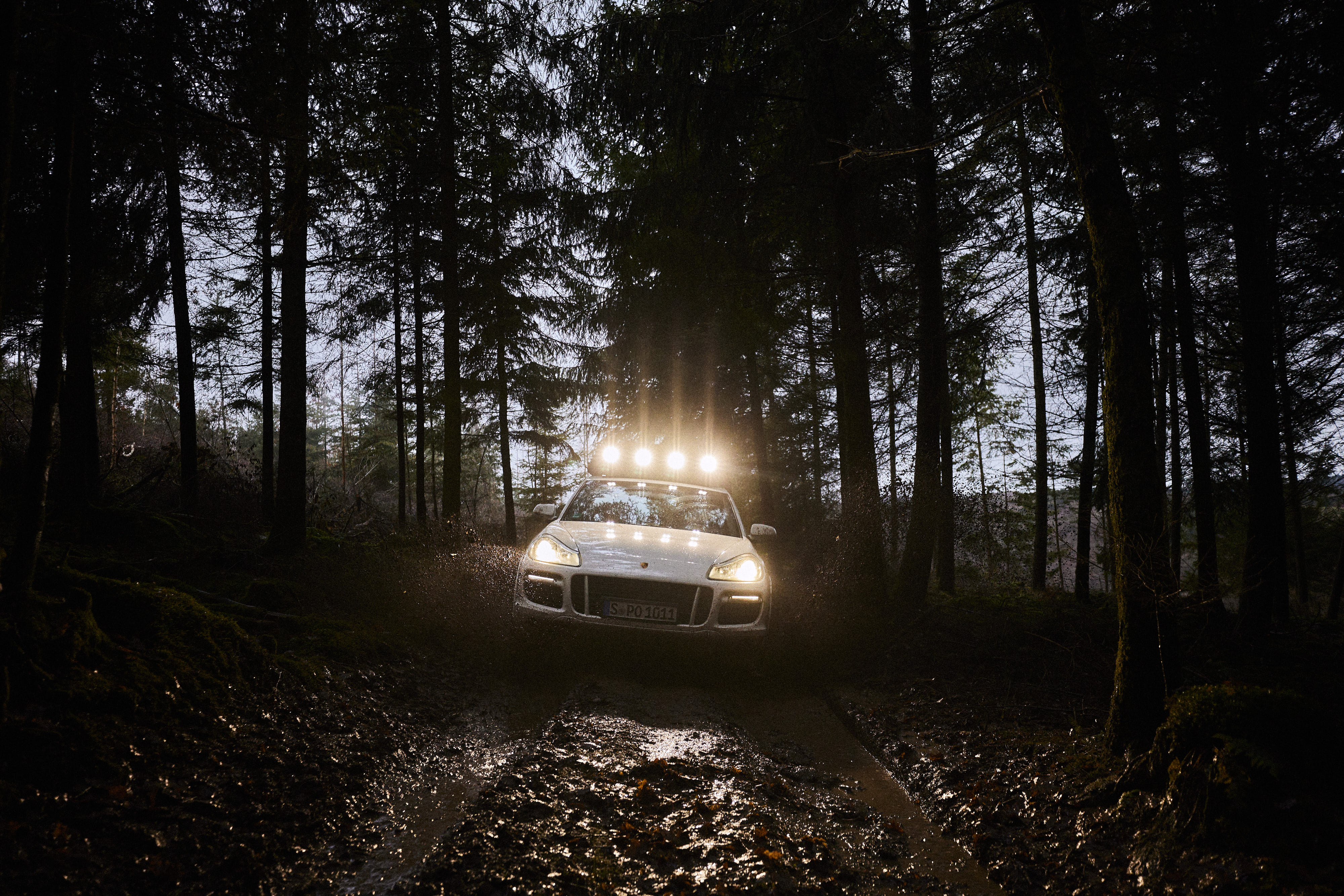 First-generation Cayenne with roof spotlights driving through dark woods