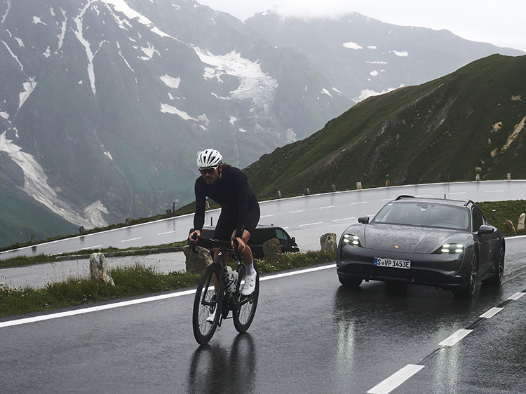 Man cycling up mountain with Porsche Taycan Turbo Cross Turismo