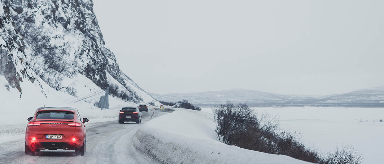 Three Porsche drive on snow and ice street next to a frozen lake