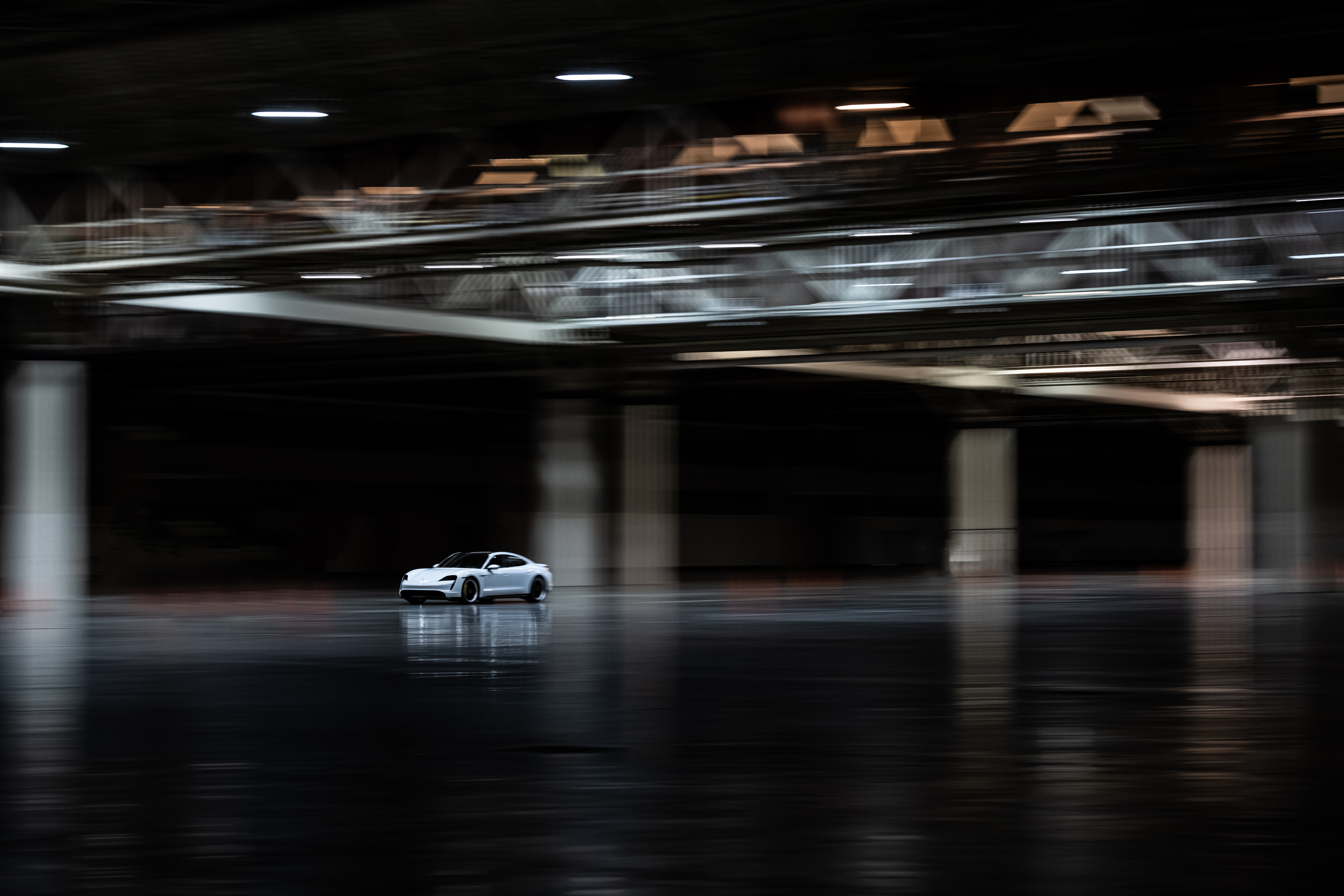 Widescreen shot of white Taycan driving in dark exhibition hall