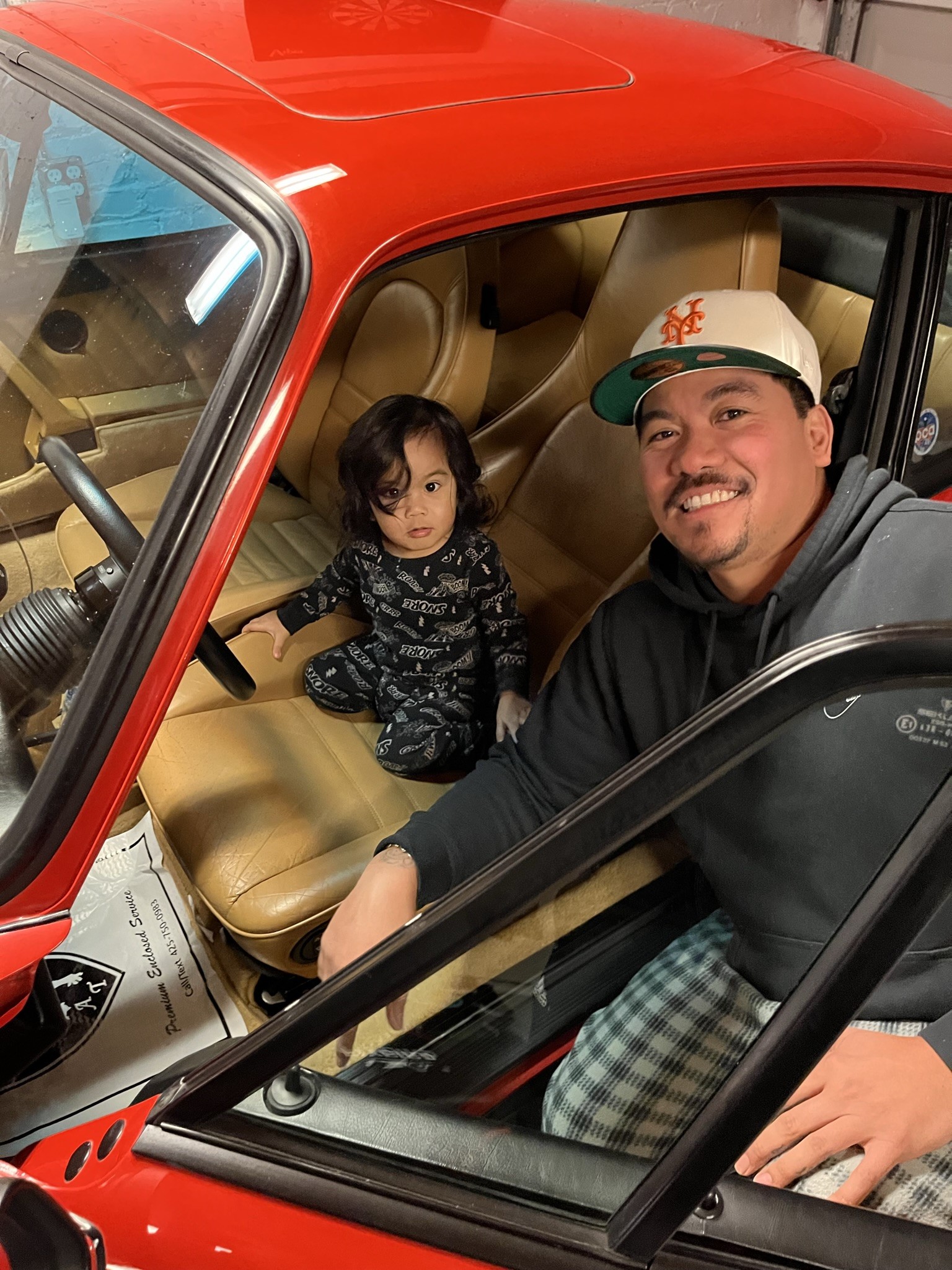 Man leans into Porsche 911 with small boy in seat