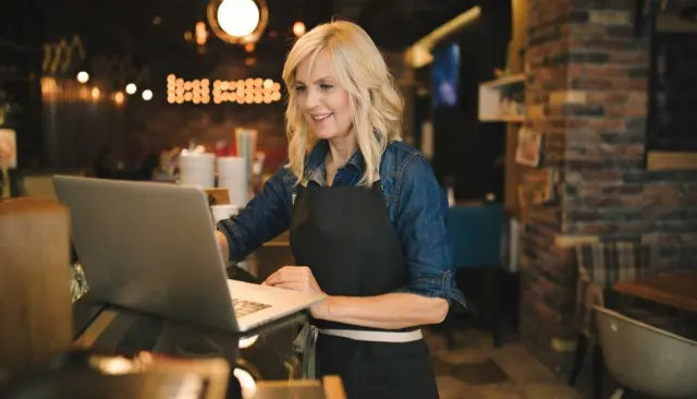 Woman standing at the counter in a restaurant looking at a laptop