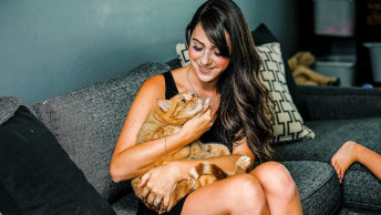 Woman cuddling an orange tabby cat sitting on the couch