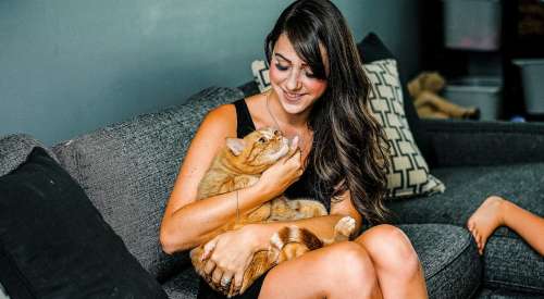 Woman cuddling an orange tabby cat sitting on the couch