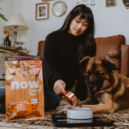 Woman sitting on floor in living room scooping NOW FRESH kibble for dog