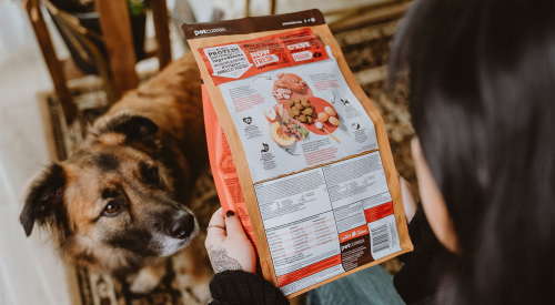 Dog watching owner read ingredient list on dog food bag