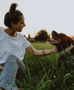 Woman sitting in grass with Chocolate Lab dog