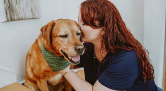 Woman with red hair kissing Labrador dog