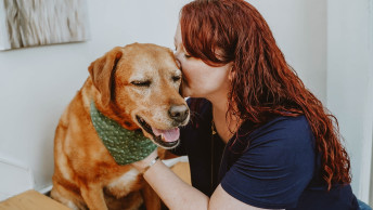 Woman with red hair kissing Labrador dog