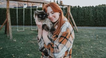 Red haired woman hugging cat outside