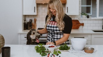Woman in apron at kitchen counter petting dog