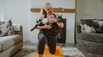 Shelley holding black and white cat in warrior yoga pose