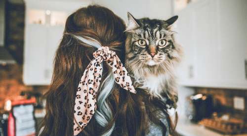 Woman with bandana in her hair holding long haired cat looking over her shoulder