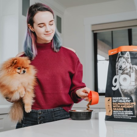 Owner holding Pomeranian pouring GO! SOLUTIONS kibble into bowl