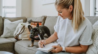 Woman writing notes beside dog on couch
