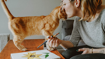 Cat bunting heads with woman painting a flower