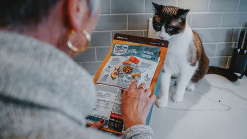 Cat watching owner read ingredient list on cat food bag